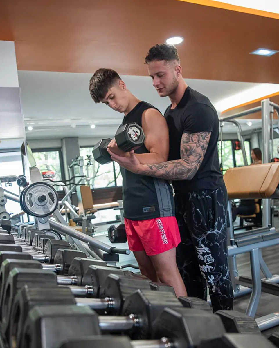 Niccolò Lucacci segue un atleta durante un curl con manubrio in sala pesi